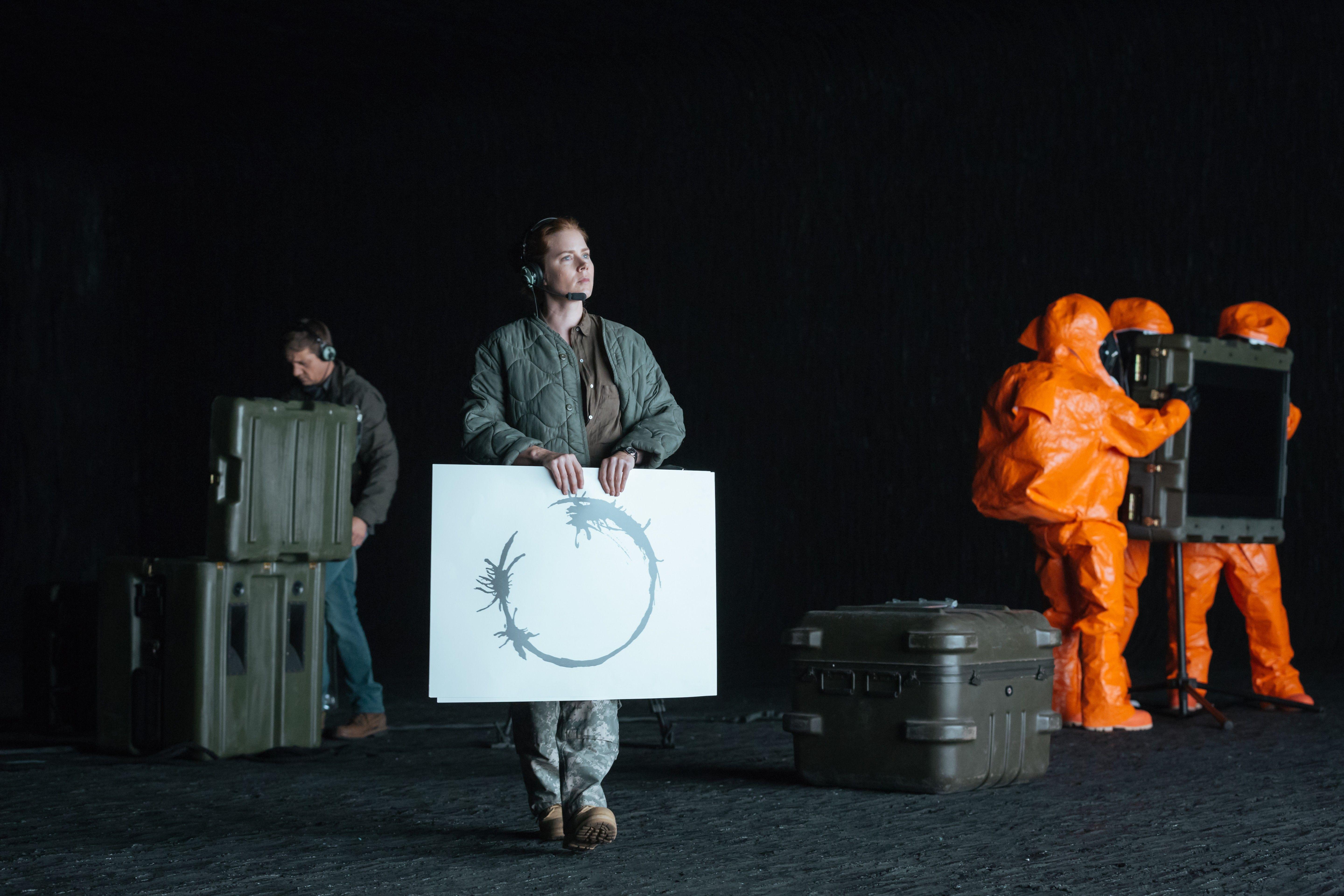 Louise on set holding a board with a heptapod logogram, next to the film crew